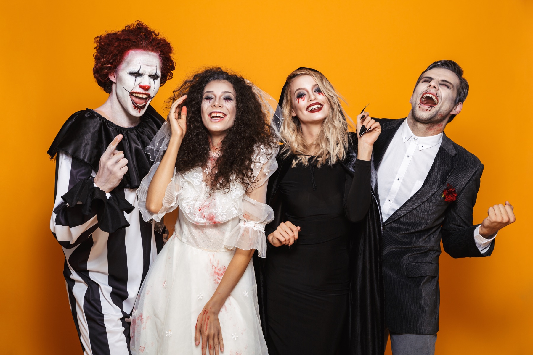 Four adults showing off theatrical Halloween costumes against an orange background