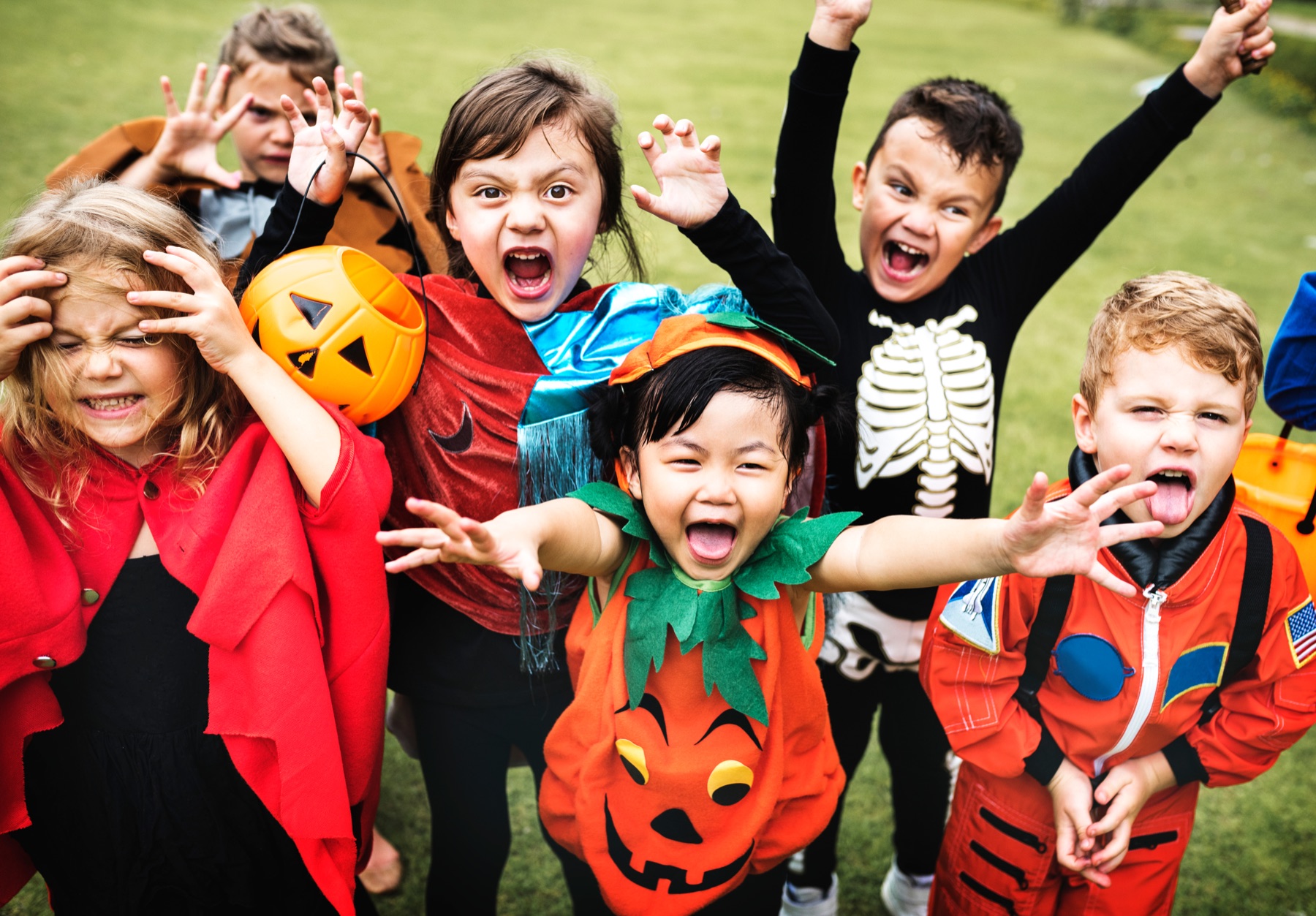 A lively group of children wearing colorful Halloween costumes outdoors