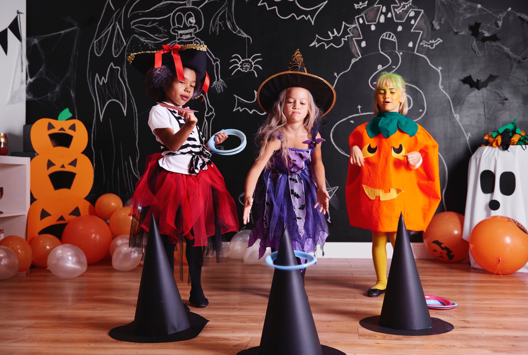 Three children in pirate, witch, and pumpkin costumes playing a party game